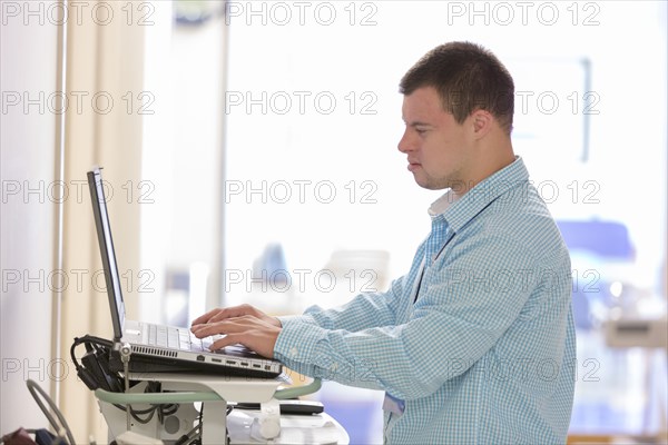 Caucasian man with Down Syndrome working on laptop in hospital