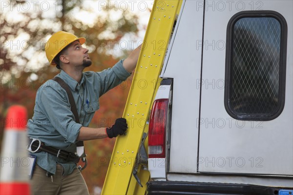 Caucasian worker loading ladder on truck