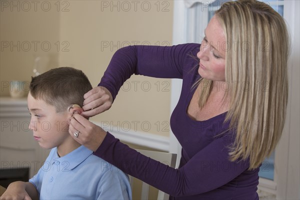 Caucasian mother fitting deaf son with hearing aid