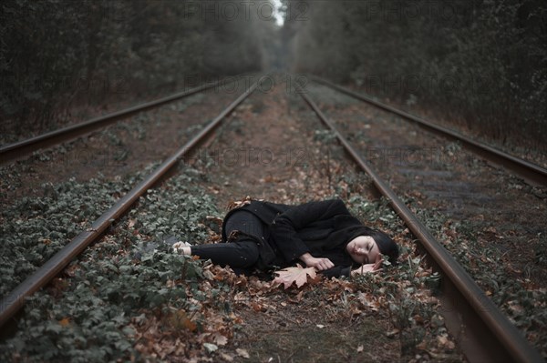Caucasian woman laying between railroad tracks