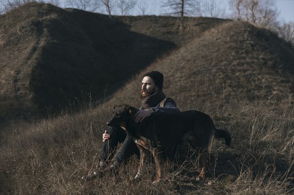 Caucasian man sitting on hill petting dog