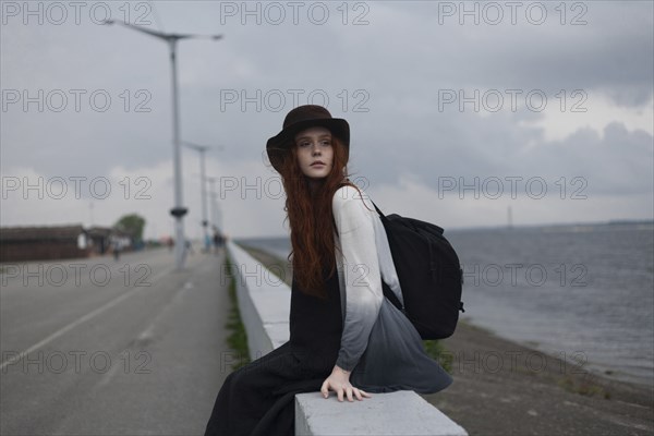 Serious Caucasian woman sitting on wall near ocean