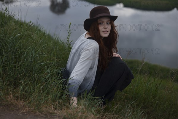 Serious Caucasian woman sitting on hill near lake