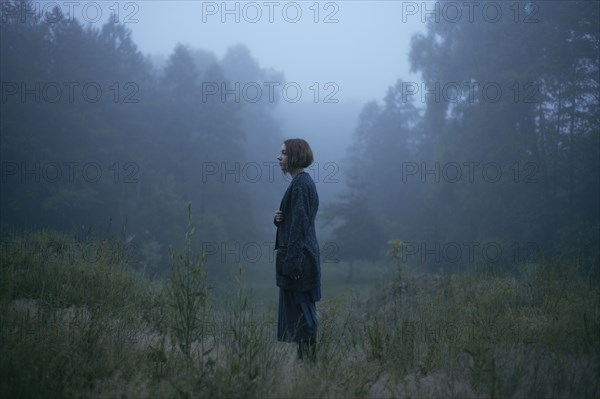 Pensive woman standing in fog in forest