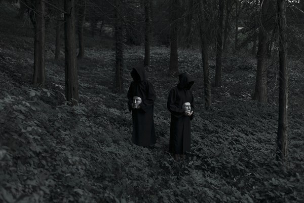 People wearing black robes and holding white masks in forest