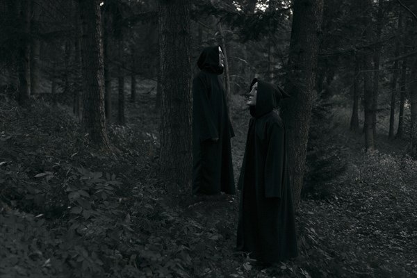People wearing black robes and white masks standing in forest