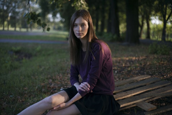 Serious Caucasian woman sitting on wooden pallet in park