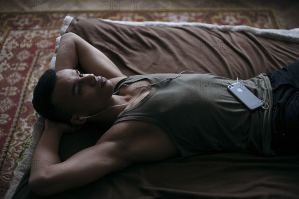 Black man laying on bed listening to music on cell phone