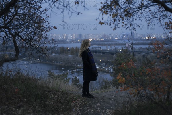 Pensive Caucasian woman standing near urban waterfront at night