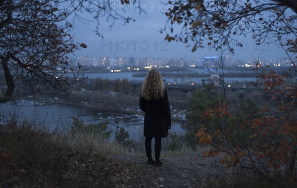 Pensive Caucasian woman standing near urban waterfront at night