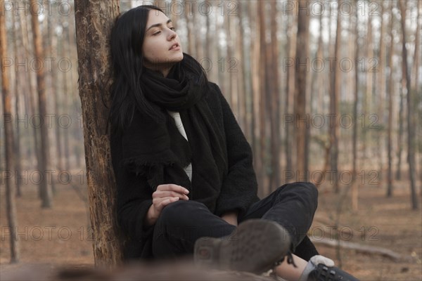 Pensive Caucasian woman sitting on log in forest