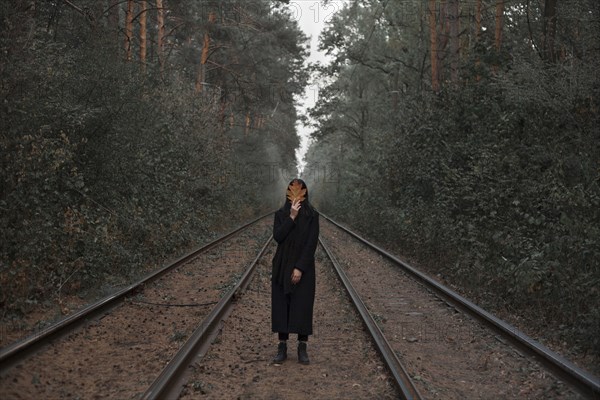 Caucasian woman holding autumn leaf on train tracks in forest