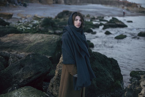 Caucasian woman wearing scarf near rocks at ocean