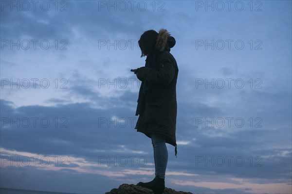 Caucasian woman wearing coat texting on cell phone at sunset