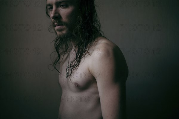 Pensive Caucasian man with long hair and bare chest