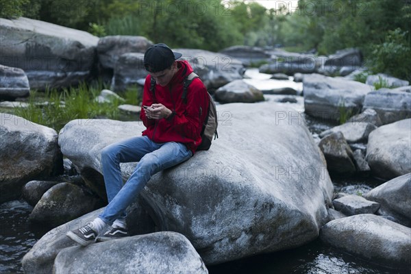 Caucasian man sitting on rock in river texting on cell phone