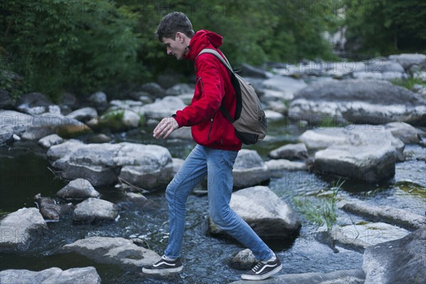 Caucasian man walking on rocks crossing river