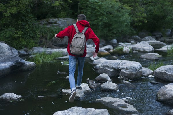 Caucasian man walking on rocks crossing river