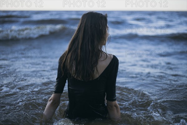 Caucasian woman wearing dress wading in ocean