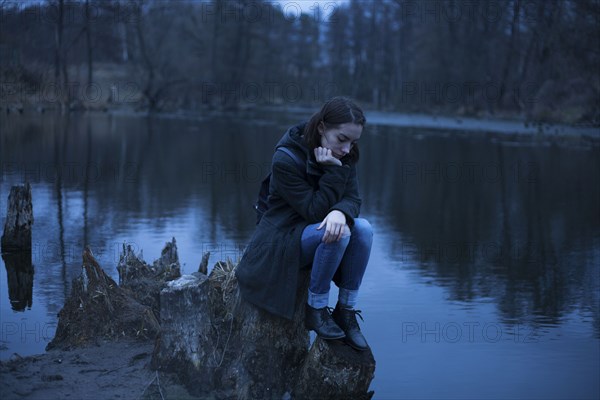 Caucasian woman sitting on tree stump near river thinking