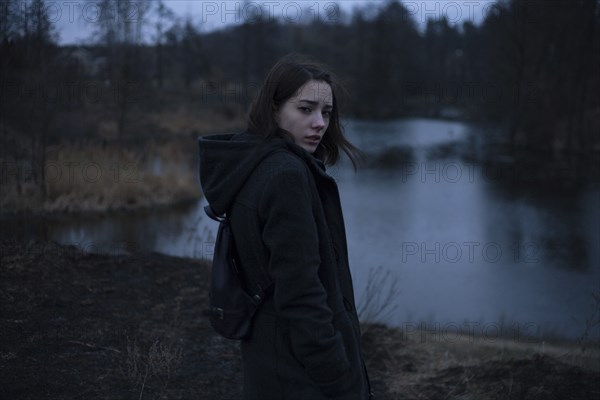 Portraits of serious Caucasian woman standing near river at night