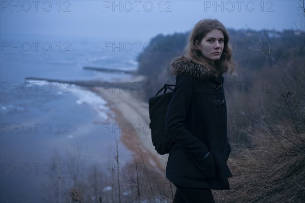 Caucasian woman wearing coat on cliff near ocean