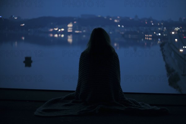 Caucasian woman sitting near waterfront at night