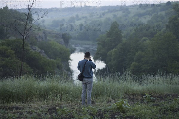 Caucasian man standing on hill photographing river