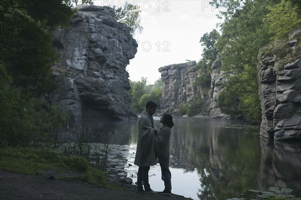 Caucasian couple wrapped in blanket holding hands near river