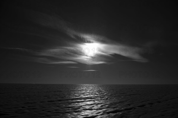 Moon shining behind cloud over ocean