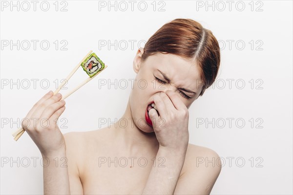 Caucasian woman holding sushi with chopsticks and holding nose