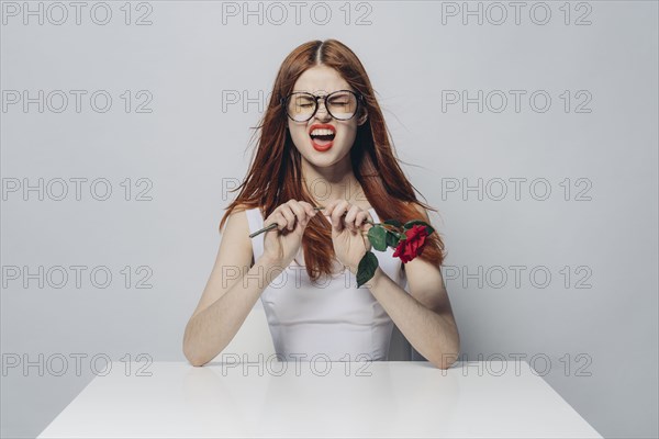 Caucasian woman sitting at windy table snapping stem of rose