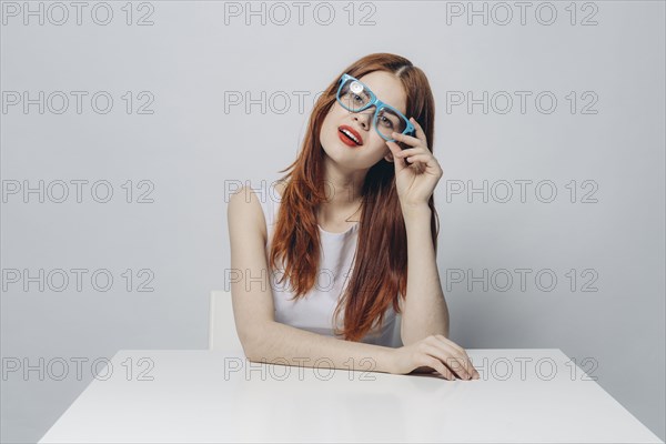 Pensive Caucasian woman sitting at table wearing blue eyeglasses