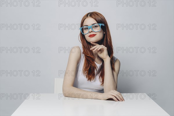 Pensive Caucasian woman sitting at table wearing blue eyeglasses