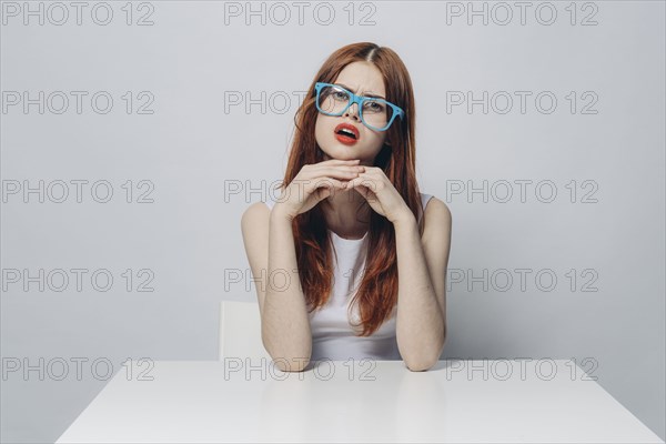 Angry Caucasian woman sitting at table wearing blue eyeglasses