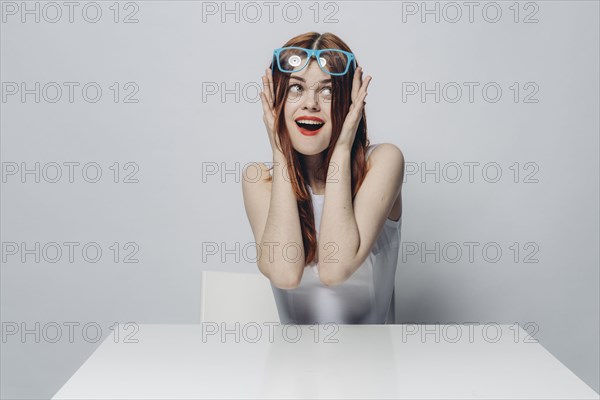 Happy Caucasian woman sitting at table lifting blue eyeglasses