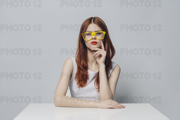 Serious Caucasian woman sitting at table wearing yellow eyeglasses