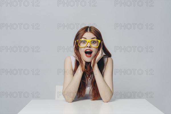 Surprised Caucasian woman sitting at table wearing yellow eyeglasses