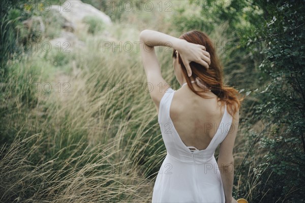 Caucasian woman standing in tall grass with hand in hair