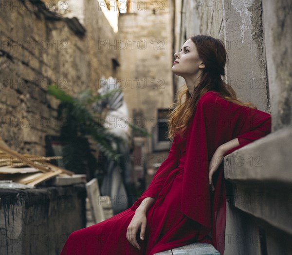 Caucasian woman wearing red dress sitting on bench in alley