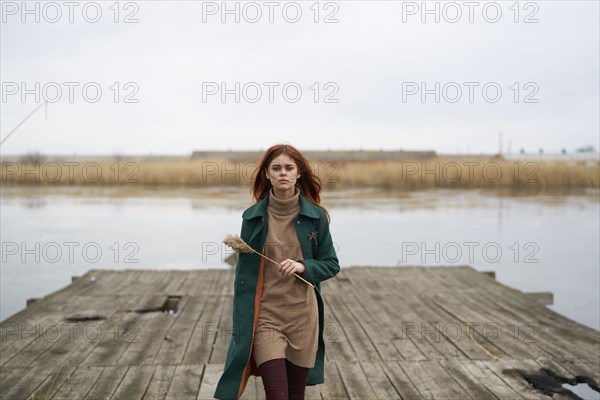 Serious Caucasian woman walking on dock holding stalk of grass