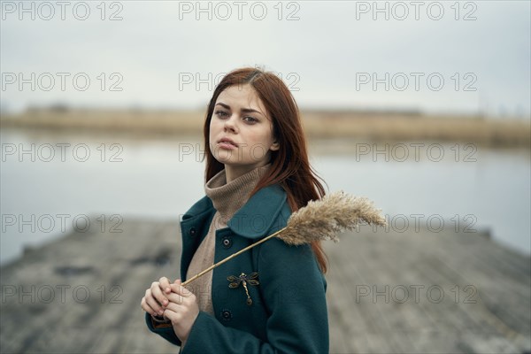 Serious Caucasian woman standing on dock holding stalk of grass