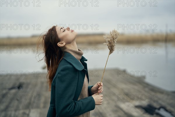 Carefree Caucasian woman standing on dock holding stalk of grass