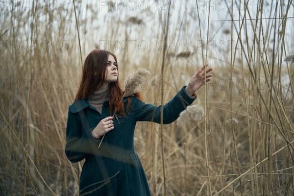 Caucasian woman standing in field touching stalk of grass