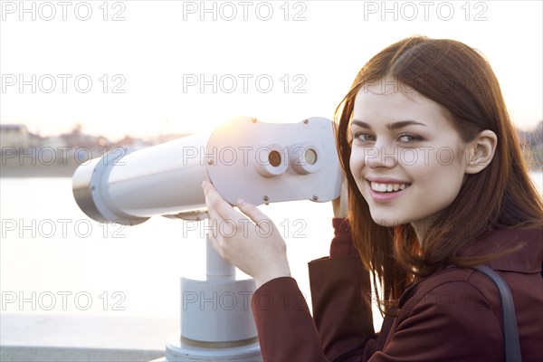 Smiling Caucasian woman using binoculars at waterfront