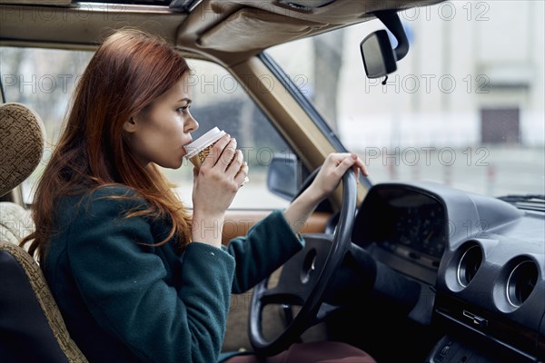 Caucasian woman driving car and drinking coffee