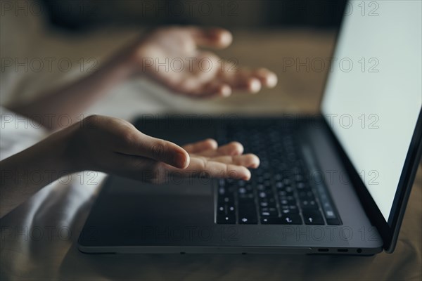 Hands of Caucasian woman gesturing at laptop in bed