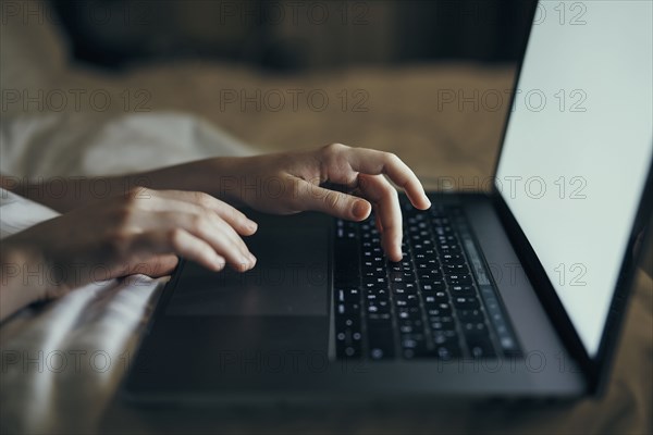 Hands of Caucasian woman typing on laptop in bed