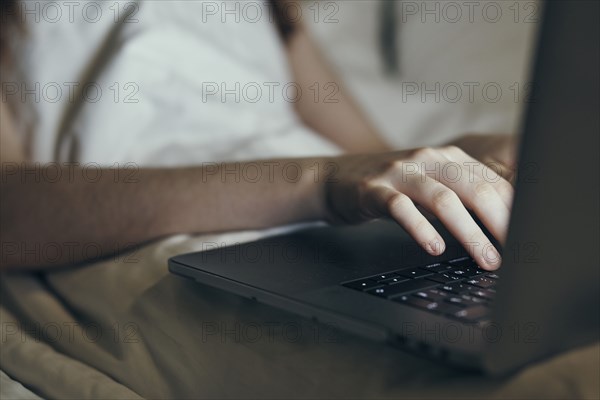 Hands of Caucasian woman typing on laptop in bed