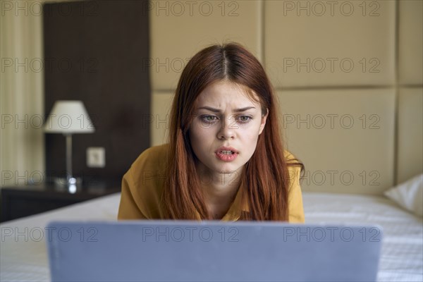 Frustrated Caucasian woman laying on bed using laptop